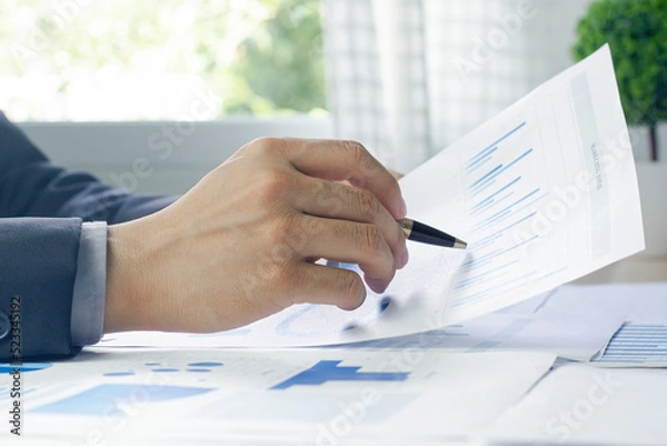 Fototapeta Close up of a Business man hand analyzing chart and graph showing changes on the market.