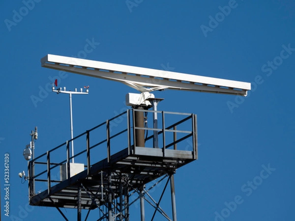 Fototapeta A rotating antenna in white on a blue sky background in bright daylight