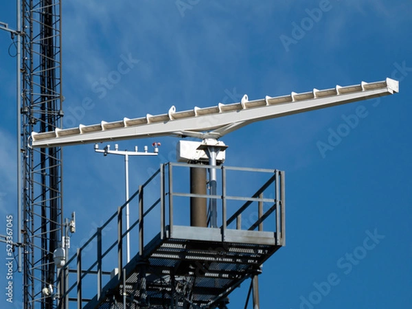 Fototapeta A rotating antenna in white on a blue sky background in bright daylight