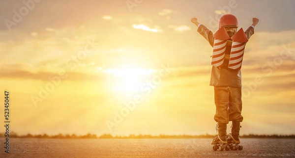 Obraz Little boy in a rocketman costume on roller skates at sunset. Ñhild imagines himself as a superhero and dreams of flying in a backpack with rockets.