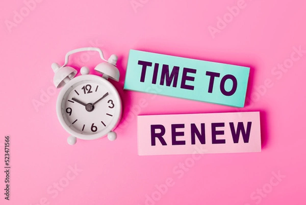 Fototapeta White alarm clock isolated on vivid pink background with text TIME TO RENEW, written on paper notes. Closeup of a personal agenda, top view. Motivational quote