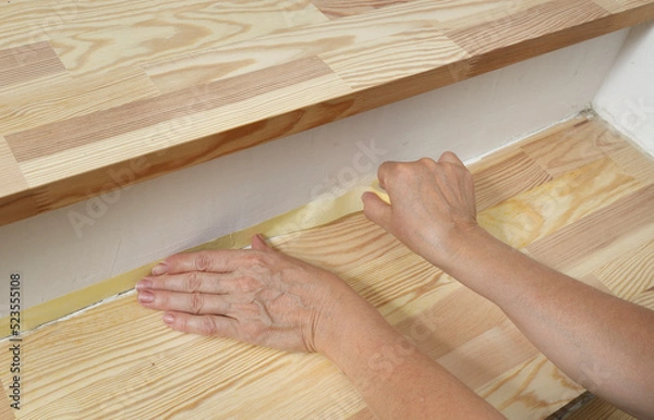 Obraz Worker preparing pine wooden plank stairs for painting or varnishing, workers hand and paper masking tape