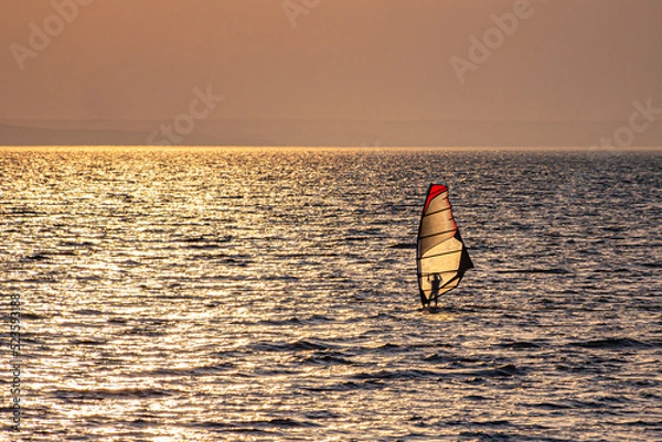 Obraz A lonely windsurfer swims towards the sun