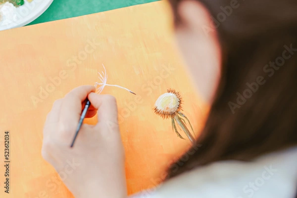 Fototapeta  woman painting dandelion flower seeds with left hand. creative occupayion. Left handed people day. over the shoulder view
