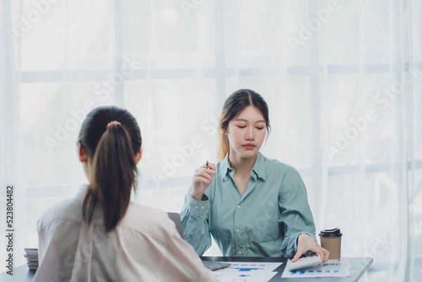 Fototapeta Two young Asian businesswoman discuss investment project working and planning strategy. Business people talking together with laptop computer at office.