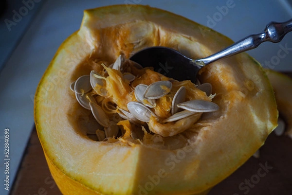 Fototapeta Sliced ​​fresh raw pumpkin with a spoon in the middle. The process of extracting seeds from a pumpkin