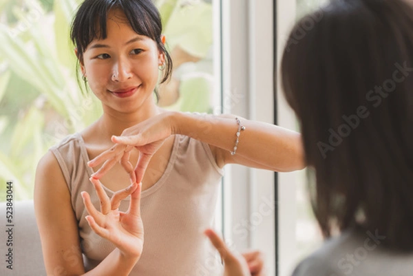 Obraz Young attractive Asian women using sign hand finger language conversation with deaf person. Cheerful happy using nonverbal communication to persons with disabilities.