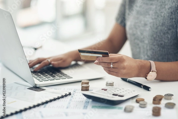 Fototapeta Budget with technology for online shopping and working indoors. Closeup of financial advisor counting money on laptop in the office. Businesswoman holding card, coins and calculator on table.