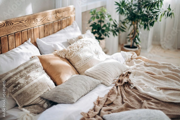 Obraz Pillows and handmade textiles on a large wooden bed in a sunny boho bedroom. Empty space