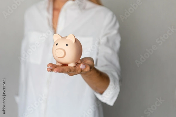 Obraz female hands puts a coin in a pink piggy bank. The concept of saving money or savings, investment