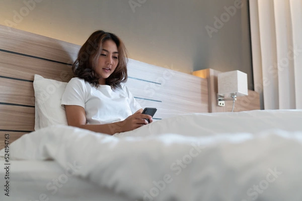 Obraz Young woman using smartphone on bed