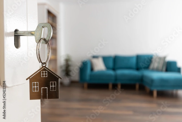Fototapeta Open door to a new home. Door handle with key and home shaped keychain. Mortgage, investment, real estate, property and new home concept