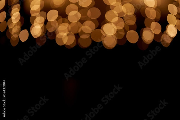 Fototapeta Golden defocused bokeh lights on top of the image on an isolated black background. Abstract magic background with bokeh effect, golden glitter for Christmas. Overlay for your design