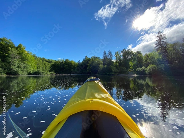 Fototapeta Kayak gonflable sur un lac paisible l'été. Pointe d'un canot jaune avec rame sur une rivière entourée de montagnes et d'une forêt. Pagayer sur l'eau calme. 