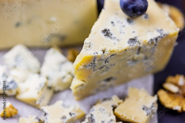 Fototapeta Tasty blue cheese served with grape and green on a wooden background. Dorblu cheese pieces