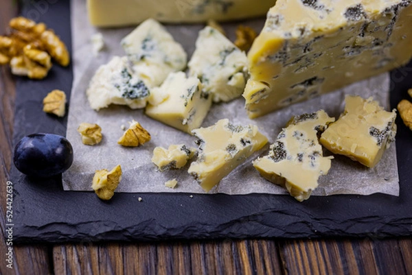 Fototapeta Tasty blue cheese served with grape and green on a wooden background. Dorblu cheese pieces