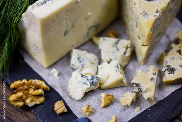 Fototapeta Tasty blue cheese served with grape and green on a wooden background. Dorblu cheese pieces
