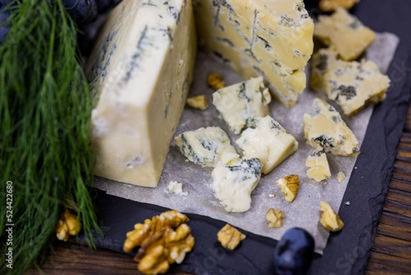 Fototapeta Tasty blue cheese served with grape and green on a wooden background. Dorblu cheese pieces