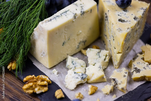 Fototapeta Tasty blue cheese served with grape and green on a wooden background. Dorblu cheese pieces