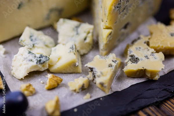 Fototapeta Tasty blue cheese served with grape and green on a wooden background. Dorblu cheese pieces