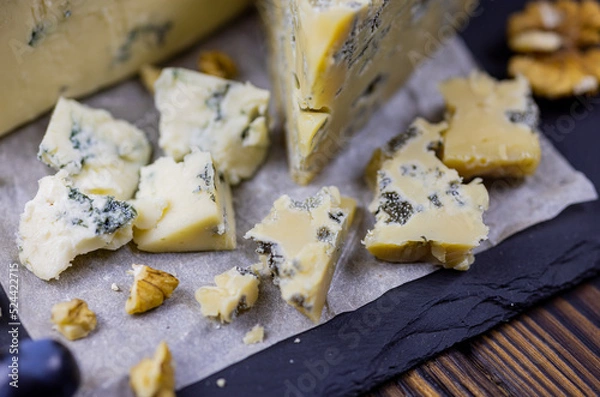 Fototapeta Tasty blue cheese served with grape and green on a wooden background. Dorblu cheese pieces