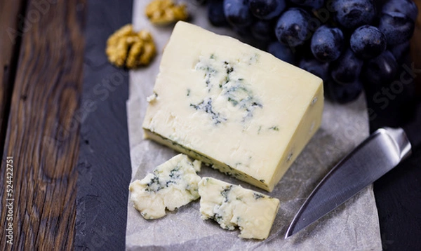 Fototapeta Tasty blue cheese served with grape and green on a wooden background. Dorblu cheese pieces