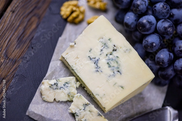 Fototapeta Tasty blue cheese served with grape and green on a wooden background. Dorblu cheese pieces