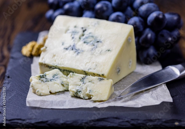 Fototapeta Tasty blue cheese served with grape and green on a wooden background. Dorblu cheese pieces