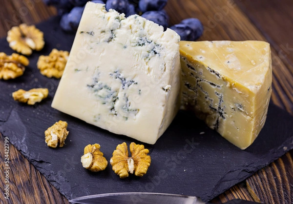 Fototapeta Tasty blue cheese served with grape and green on a wooden background. Dorblu cheese pieces