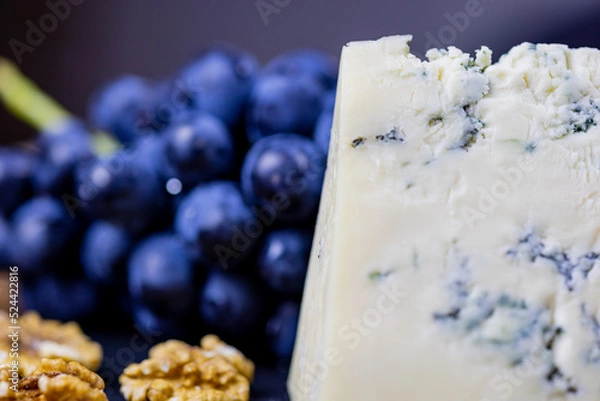 Fototapeta Tasty blue cheese served with grape and green on a wooden background. Dorblu cheese pieces