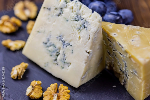 Fototapeta Tasty blue cheese served with grape and green on a wooden background. Dorblu cheese pieces