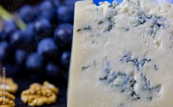 Fototapeta Tasty blue cheese served with grape and green on a wooden background. Dorblu cheese pieces