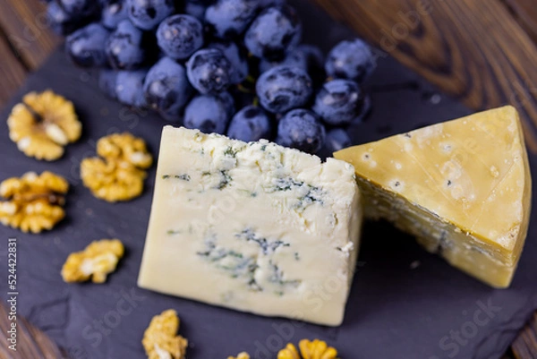 Fototapeta Tasty blue cheese served with grape and green on a wooden background. Dorblu cheese pieces