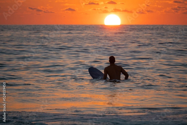 Fototapeta Silhouette of Surfer waiting on the line up for a wave at sunrise or sunset