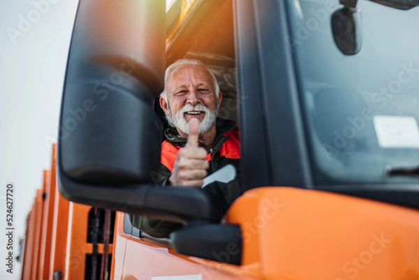 Obraz Senior garbage removal worker driving a waste truck. He is showing thumb up.