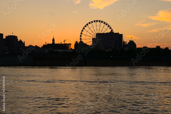 Fototapeta Montreal Grand Ferris Wheel in Old Port at sunset. Reflections of sun rays on Saint Laurent river with a background of cloudy blue sky