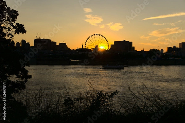 Fototapeta Montreal Grand Ferris Wheel in Old Port at sunset. Reflections of sun rays on Saint Laurent river with a background of cloudy blue sky