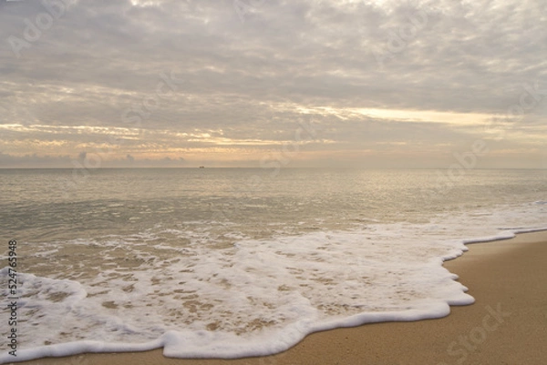 Fototapeta Morning sky with clouds from the beach. White surf on the sand with a small boat in the sea.