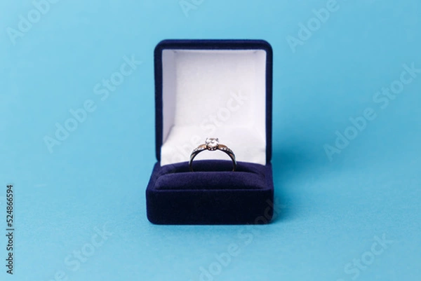 Fototapeta Jewelry, gold diamond ring in a blue box on a turquoise background, isolated.  A ring for a marriage proposal. Close-up. Front view. A place for your text.