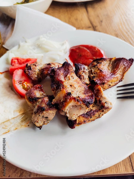 Fototapeta Meat fried on skewers. Meat fried pieces on a white plate with a fork, with tomatoes and pita bread. Appetizing.Barbecue.Vertical