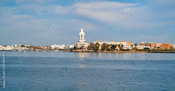 Fototapeta View of the tourist town and lighthouse of Isla Cristina from Isla del Moral with the  Carreras River near the mouth of the sea, Huelva, Andalusia, Spain