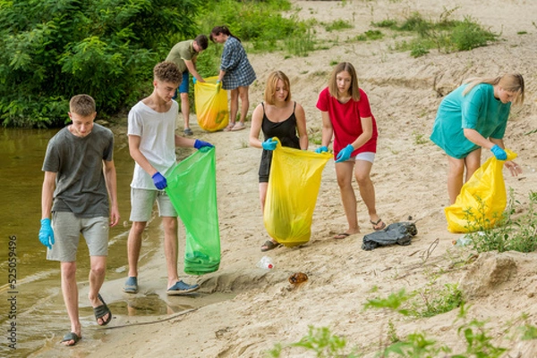 Fototapeta a team of teenagers collect garbage on the river bank