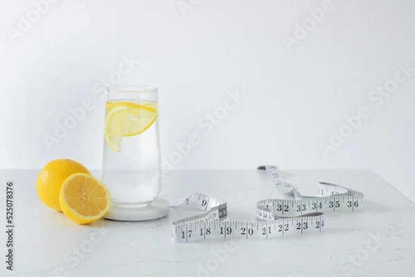 Fototapeta A glass of clean water with lemon slices, next to a fresh lemon and a centimeter. Healthy food concept. Losing weight concept.