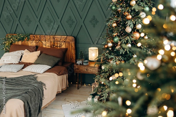 Obraz Bedroom decorated for Christmas. Bedroom interior with green walls, double bed and green Christmas tree decorated with emerald and bronze balls. View through blurred bokeh from garland lights. Nobody
