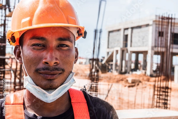Fototapeta Latino indigenous blue collar worker in the construction of a work looking at the camera