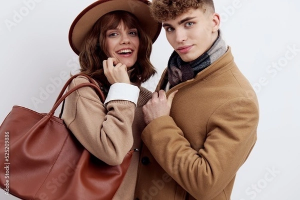 Fototapeta a close horizontal photo of a beautiful, stylish couple in autumn clothes. A woman stands in a hat and holds a bag on her shoulder, holding her hand near her face