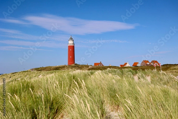 Fototapeta The lighthouse of the island of Texel in The Netherlands surrounded by tall sand dunes in beautiful sunlight.