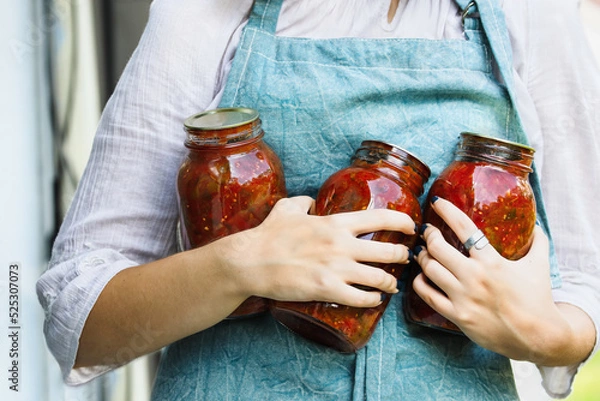 Fototapeta Woman's hands holding homemade canned quart mason jars of tomato salsa. Selective focus with blurred background.