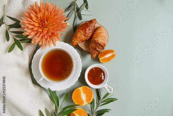 Fototapeta Cup of tea with jam and oranges on the pastel green background. Frame. Stay healthy in flu winter autumn days. Autumn fall tea composition with empty place for text. Calm cozy atmosphere. Village vibe