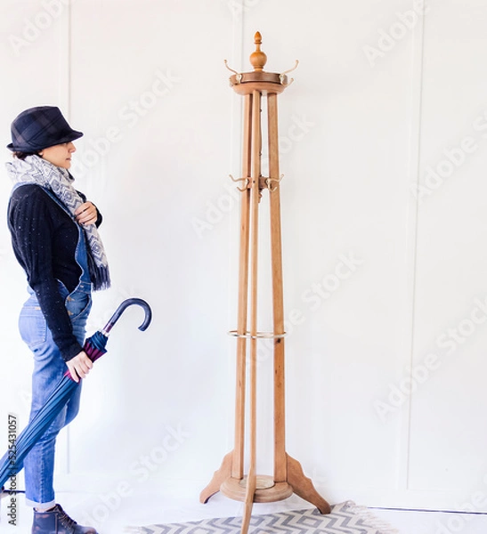 Obraz Portrait of a Caucasian woman next to a wooden coat rack preparing to hang her clothes on it.